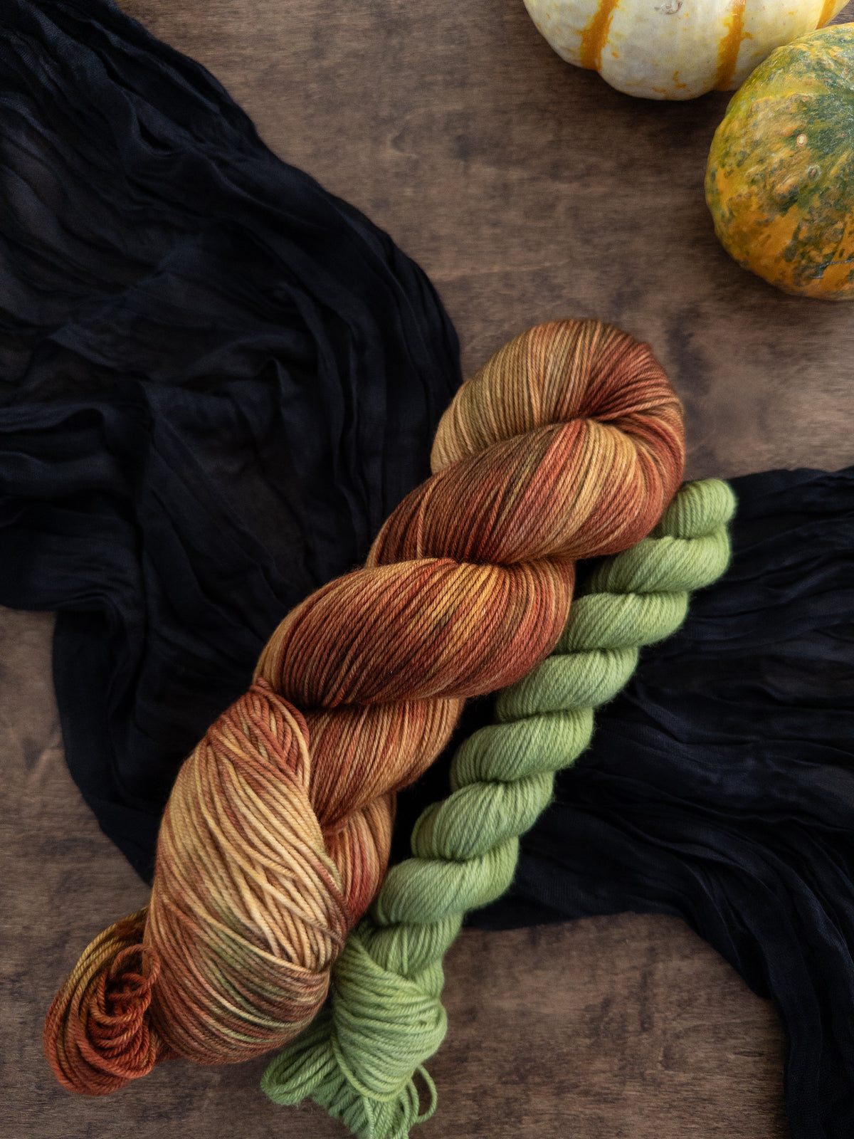 The sock set with a variegated skein that is gold, red, brown, and green alongside an apple green mini skein.